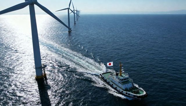 Tugboat navigating japanese-flag wake along offshore wind farm, aerial renewable energy
