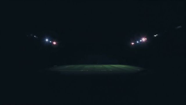 Empty illuminated gridiron under stadium floodlights at night with moody dramatic shadows