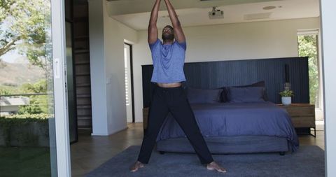 Mature man stretching in modern minimalist bedroom with balcony view and ceiling projector