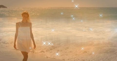 Sunlit woman walking along golden shoreline in white sundress with sparkling bokeh and sunset glow