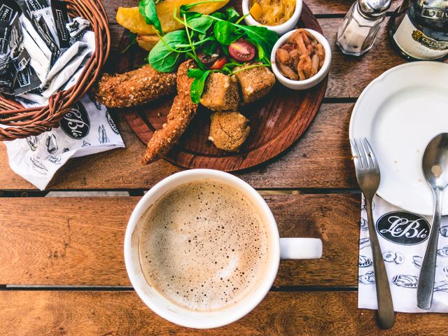 Breakfast scene featuring warm cappuccino and assorted breakfast items like sausages, breadsticks, salad on wooden table. Perfect for promoting cafes, restaurants, brunch menus, food blogs, lifestyle websites.