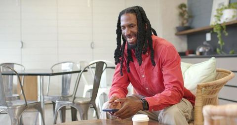 Smiling african american man using smartphone in casual coffee shop coworking lounge