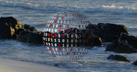 Hovering binary sphere over rocky shoreline, holographic digital globe reflecting waves
