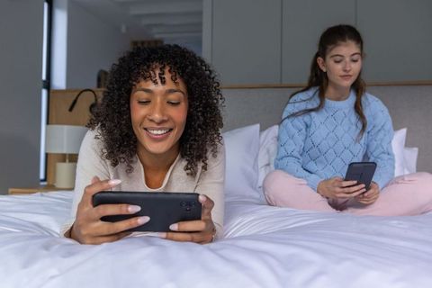 Diverse Women Relaxing on Bed Using Smartphones