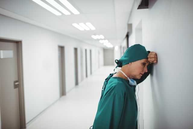 Tensed female surgeon leaning on wall in corridor of hospital