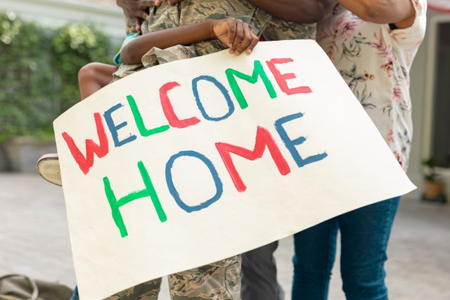 Family with welcome home placard embracing african american female soldier. unaltered, pride, military, armed forces, patriotism, homecoming, arrival.
