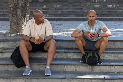 Two men sitting on stone steps drinking cold beverages after workout in urban plaza