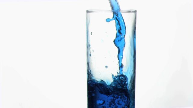 Vivid blue liquid streams into clear glass, capturing contrast and movement. Perfect for advertisements promoting beverages, water purification products, or refreshing drinks. Highlights themes of clarity, purity, and the scientific nature of fluids in motion.