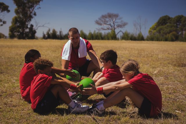 Trainer guiding children in a group exercise during an outdoor boot camp on a sunny day. Ideal for use in content related to fitness, outdoor activities, children's health, teamwork, and summer camps.