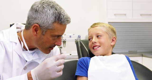 Dentist engaging with a young boy during a checkup. Ideal for use in medical and healthcare promotions, pediatric dentistry websites, health care educational materials, or any visual about dental care and children's health.