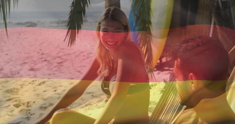 Smiling woman leaning toward man in hammock on sunlit tropical beach with surfboards
