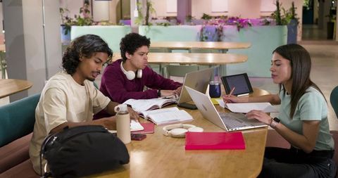 Students Collaborating at Campus Study Table with Laptops and Notebooks, Focused Group Learning