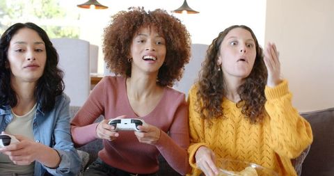 Diverse Friends Playing Video Games on Sofa Laughing and Snacking During Cozy Game Night