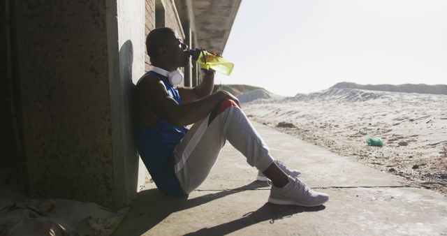 Athlete sits on ground against wall, taking a break from workout to drink water. Suitable for use in fitness, health, hydration, and sports-related projects.