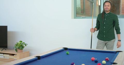 Relaxed african american man holding cue beside blue-felt pool table in modern rec room