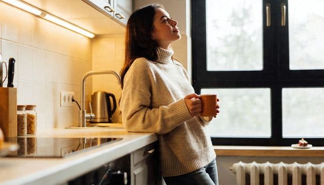 Cozy morning at home woman leaning on kitchen counter holding mug gazing through window