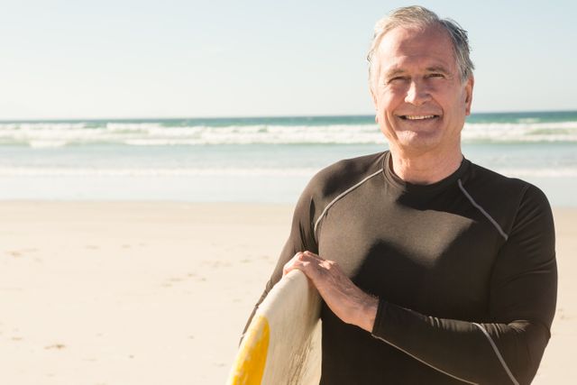 Portrait of smiling man carrying surfboard while standing on sand at beach