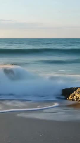 Vertical cinematic video of ocean swells rising and crashing on rocky shore leaving silky foam