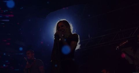 Backlit Female Lead Singer Creating Halo on Dark Concert Stage with Neon Haze