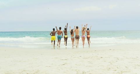 Group of Friends Running Towards Ocean in Swimwear on Beach