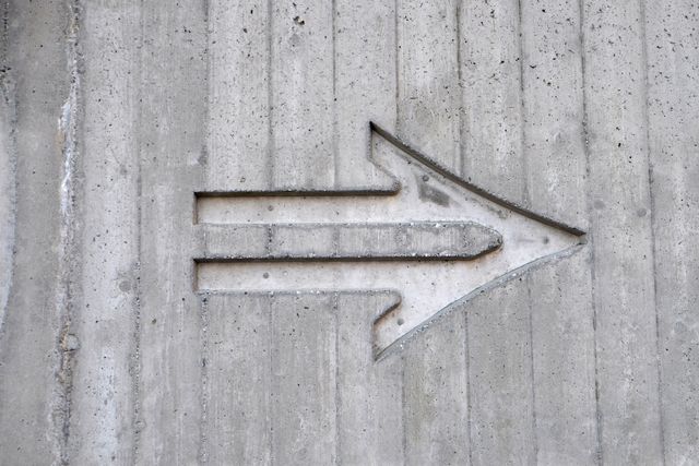 Carved arrow in concrete wall captures attention with its minimalist design. Suitable for architectural presentations, construction industry, urban environments, and directional signage projects.