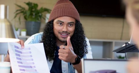 Young professional giving thumbs up while presenting purple chart to diverse team