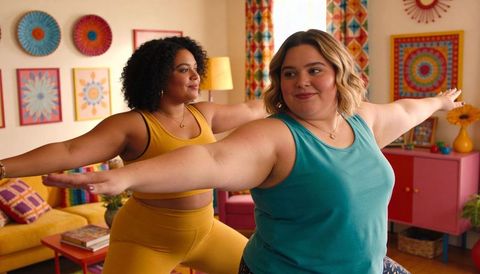 Two women practicing partner yoga in colorful living room, body positive wellness and joy