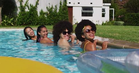 Four Friends Laughing and Relaxing in Sunlit Backyard Pool Wearing Summer Swimwear