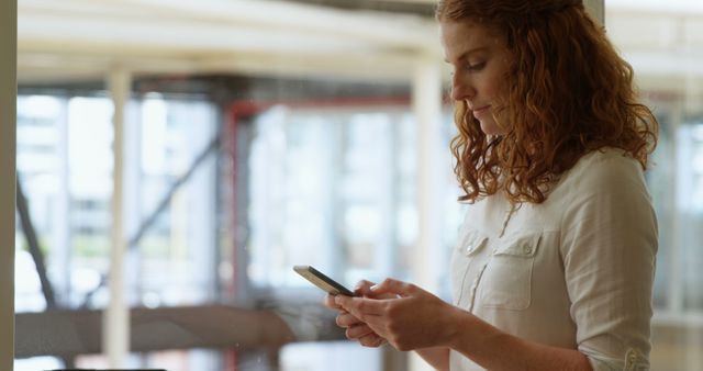 Red-haired woman texting on smartphone in office - Download Free Stock Images Pikwizard.com