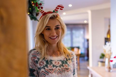 Smiling woman wearing fuzzy holiday sweater and candy-cane headband in cozy living room