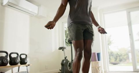Man jumping rope in bright home gym with kettlebells and exercise bike for cardio