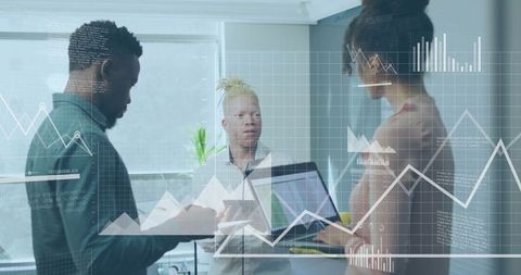 Diverse team analyzing data on laptop and tablet in sunlit modern glass office