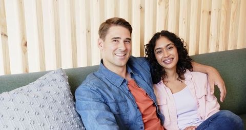 Couple sitting comfortably on a green couch, exemplifying home comfort and romantic intimacy. Textured gray pillow adds to modern living room decor. Perfect for content related to home lifestyle, modern interior design, diverse relationships, or marketing for home furniture and cozy living.