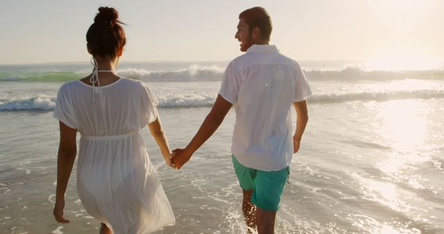 Biracial couple enjoys a beach sunset, with copy space. They share a romantic moment with waves gently breaking nearby.