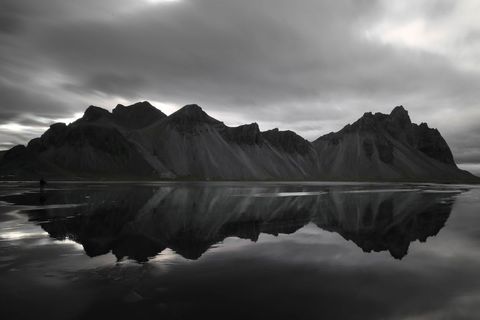 Dramatic black and white coastal mountain range reflecting on still tidal mirror under moody sky