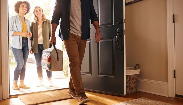 Returning family smiling carrying insulated cooler bag of gifts entering sunlit entryway