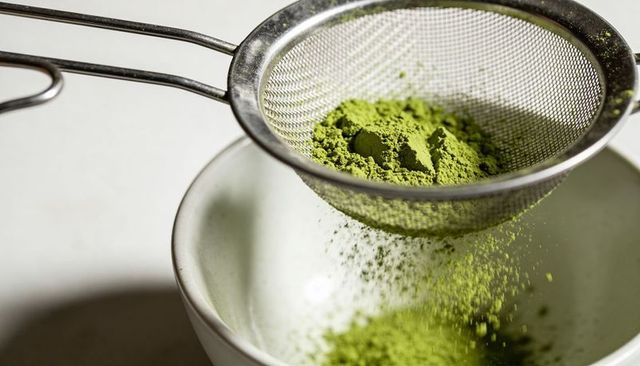 Sifting matcha powder through fine mesh sieve above ceramic bowl, green powder falling