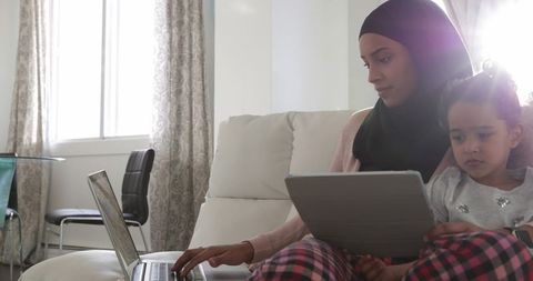 Busy Parent Wearing Hijab Multitasking with Child in Living Room