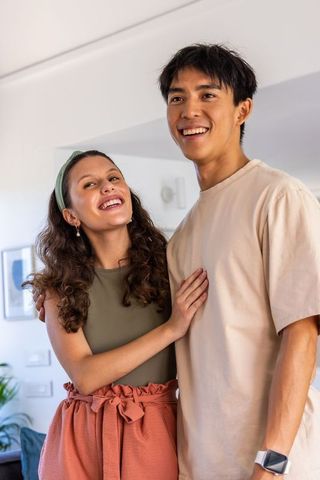 Young diverse couple smiling and looking upward in sunlit modern living room