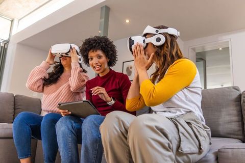Three women experiencing immersive virtual reality at home with white vr headsets, tablet