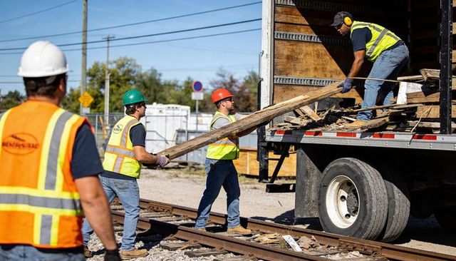 Construction crew loading debris into truck at rail yard wearing hi-vis safety gear