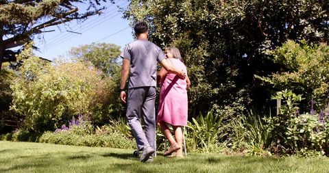 Physiotherapist Assisting Senior Woman Walking in Lush Garden