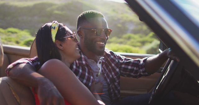 African american couple talking to each other while sitting in convertible car on road. road trip travel and adventure concept