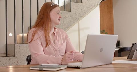 Red-haired woman working at wooden table in modern coworking space