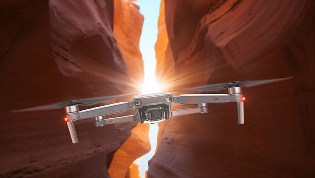 Hovering drone capturing sun flare between red slot canyon walls during golden hour