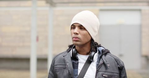 African American man wearing knit beanie, leather jacket and headphones in urban courtyard