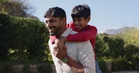 Father Giving Son Piggyback Ride in Sunlit Green Garden