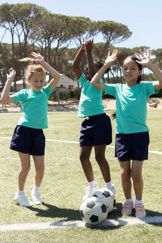 School girls celebrating soccer drill on sunny field wearing matching teal shirts