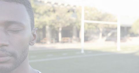 Male athlete resting with eyes closed on sunlit sports field offering calm copy space