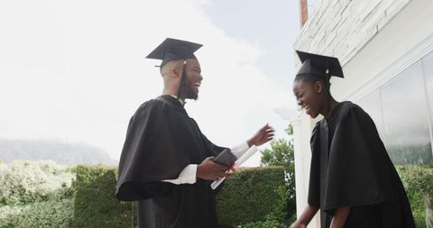 Graduating students celebrating outdoors with diplomas and gowns